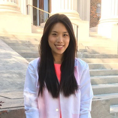 A photo of Dr. Ashley Falcone from Bella Family Dental, smiling and wearing a white coat